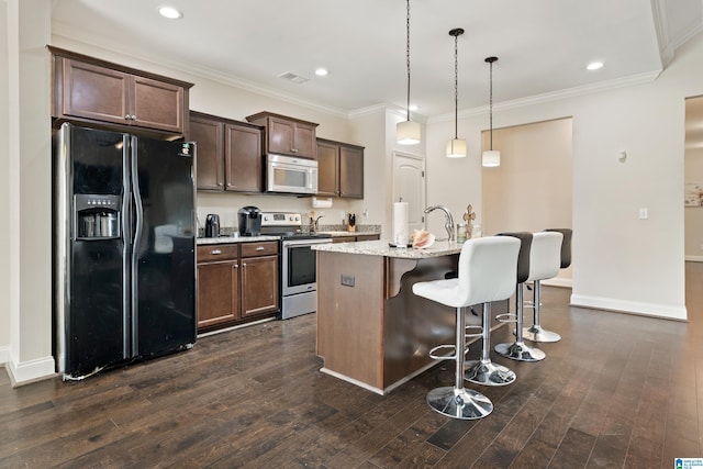 kitchen with a kitchen island with sink, dark wood-style flooring, ornamental molding, stainless steel appliances, and a kitchen bar