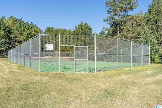 view of tennis court with a yard and fence