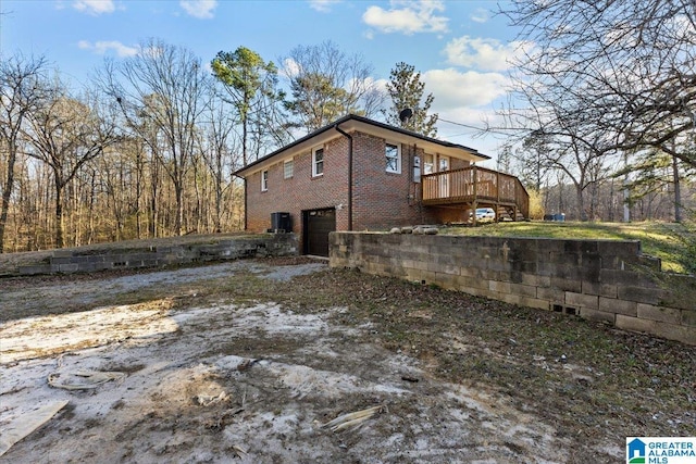 view of side of home featuring an attached garage, driveway, a deck, and brick siding