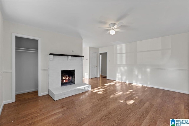 unfurnished living room with a brick fireplace, ceiling fan, baseboards, and wood finished floors