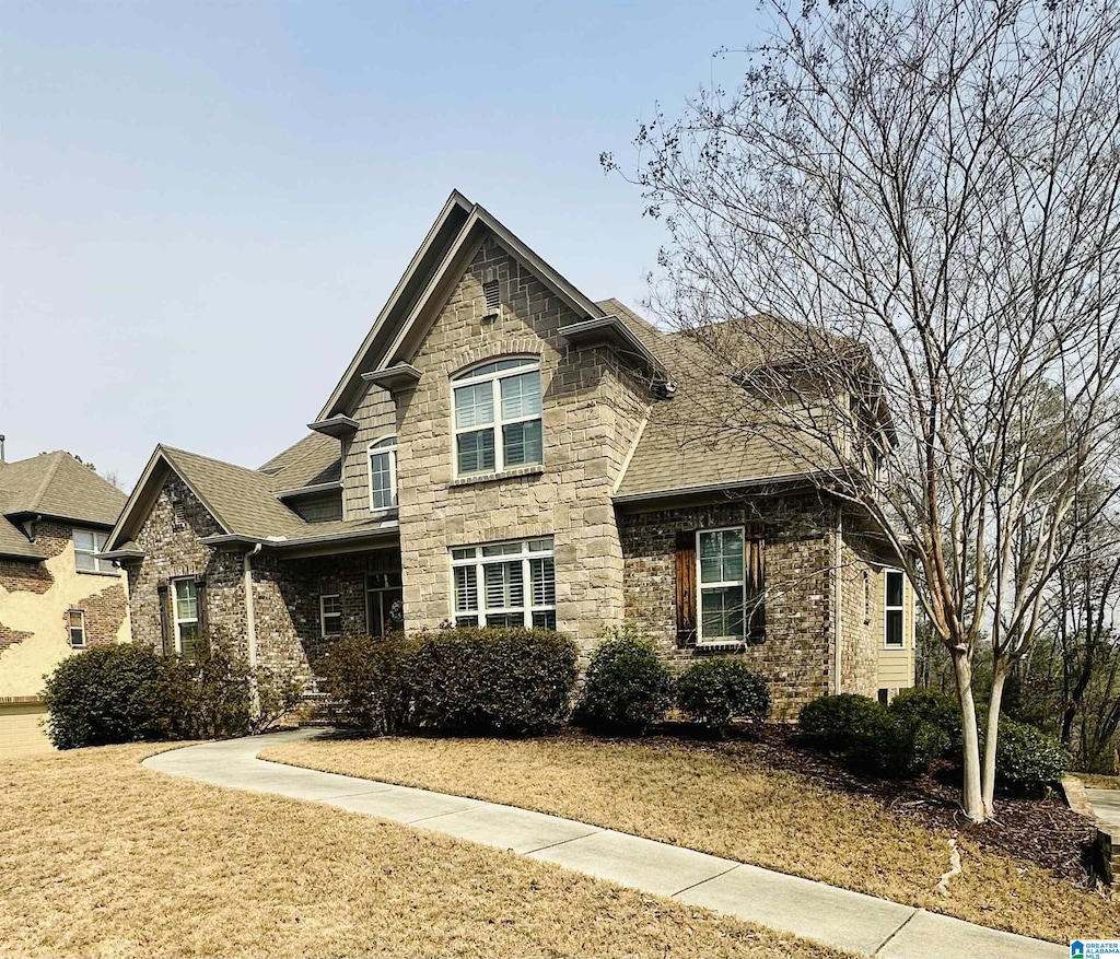 view of front facade with stone siding, roof with shingles, and a front lawn