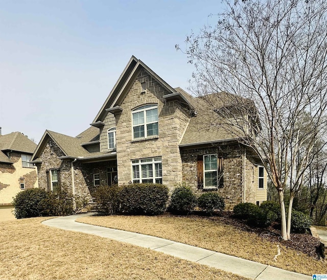 view of front of home with stone siding, roof with shingles, and a front lawn