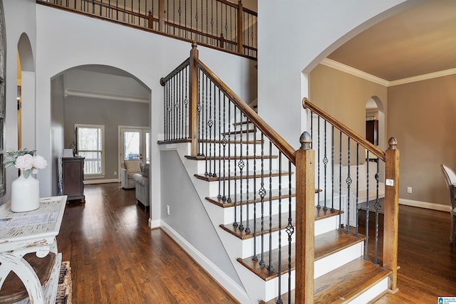 stairs featuring crown molding, wood finished floors, baseboards, and a towering ceiling