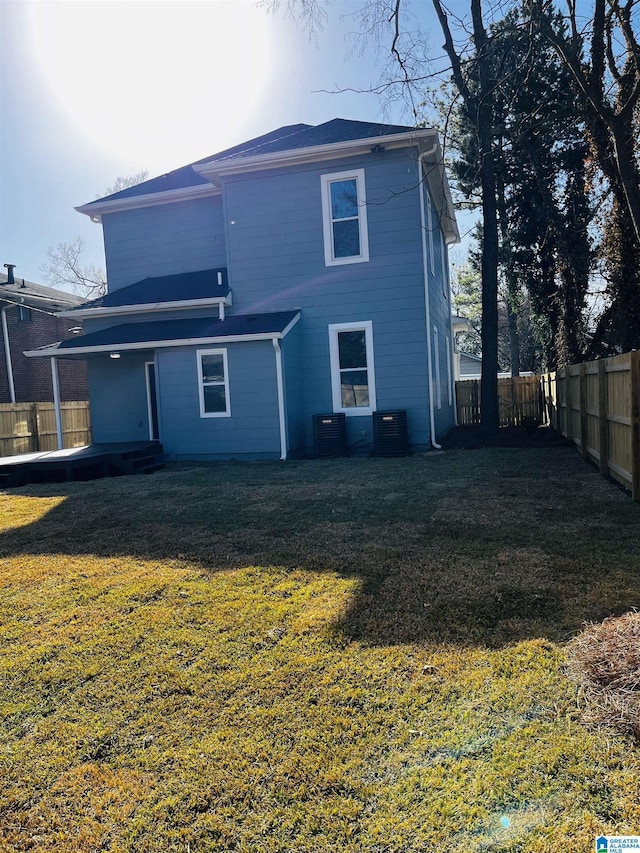 rear view of house with cooling unit, a lawn, and a fenced backyard