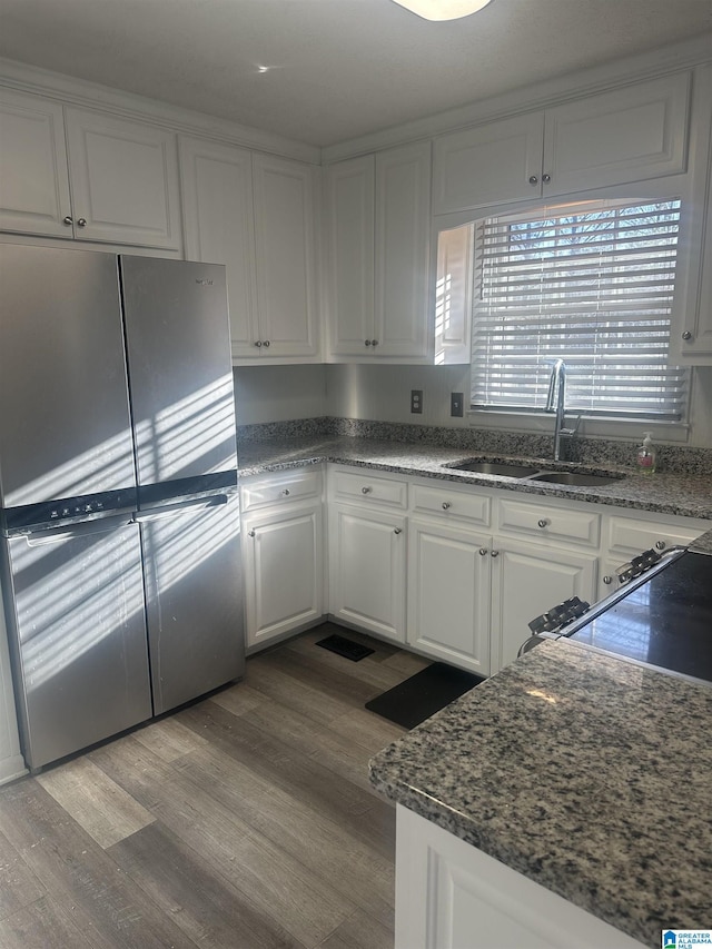 kitchen with wood finished floors, a sink, freestanding refrigerator, and white cabinetry