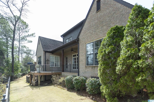 view of property exterior with a deck, ceiling fan, brick siding, a shingled roof, and stairway