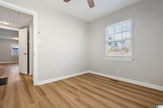 empty room with attic access, light wood-type flooring, visible vents, and baseboards