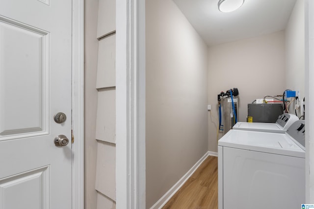 clothes washing area featuring laundry area, light wood finished floors, washing machine and clothes dryer, and baseboards