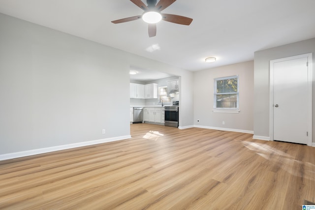 unfurnished living room featuring baseboards, a sink, light wood finished floors, and ceiling fan