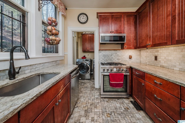 kitchen with reddish brown cabinets, appliances with stainless steel finishes, a sink, and washer and dryer