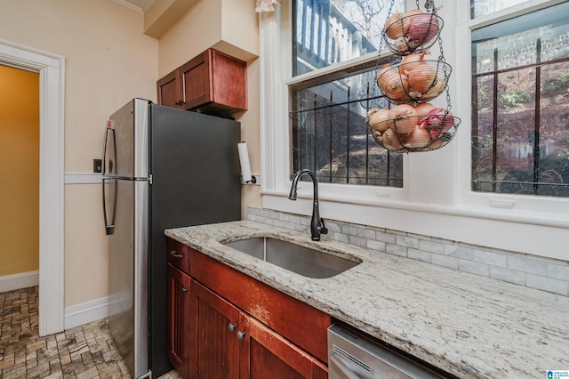 kitchen with a sink, baseboards, dark brown cabinets, appliances with stainless steel finishes, and light stone countertops