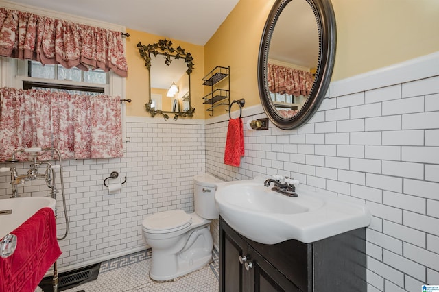 bathroom featuring tile patterned flooring, toilet, a wainscoted wall, vanity, and tile walls