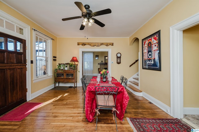 dining area with arched walkways, wood finished floors, stairs, and baseboards