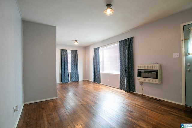 unfurnished room with wood-type flooring, visible vents, baseboards, and heating unit