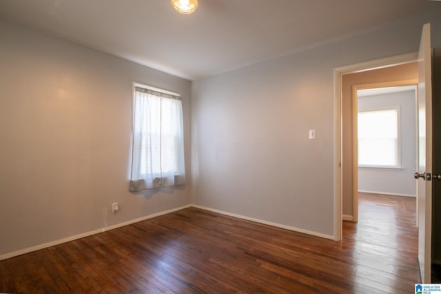 unfurnished room featuring dark wood-style flooring, plenty of natural light, and baseboards