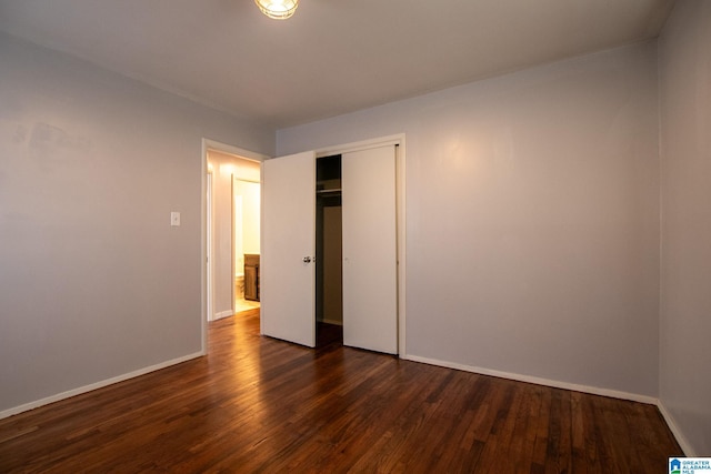 unfurnished bedroom with dark wood-style floors, a closet, and baseboards