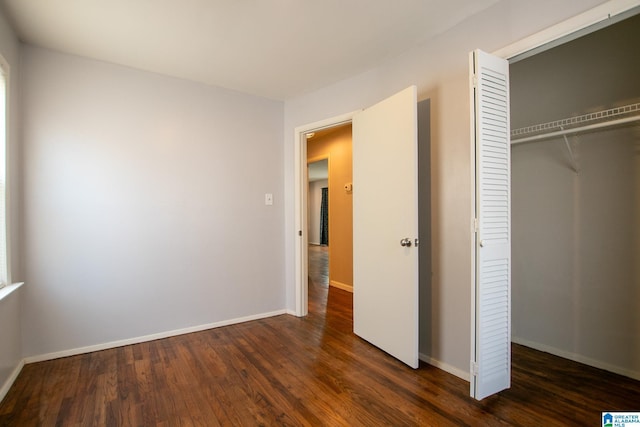 unfurnished bedroom featuring a closet, dark wood finished floors, and baseboards