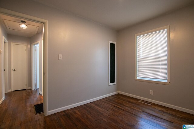 empty room featuring dark wood-type flooring, visible vents, and baseboards