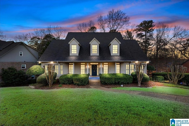 cape cod home featuring a porch, a front yard, brick siding, and roof with shingles