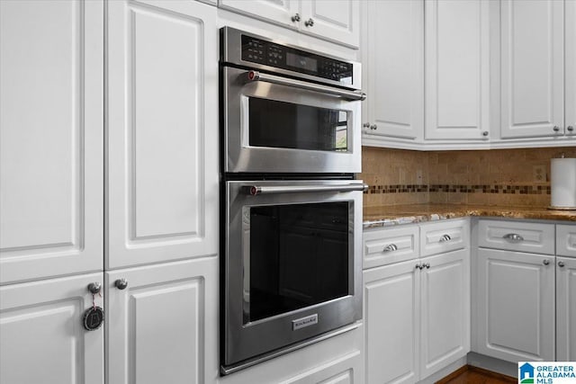 kitchen featuring light stone counters, stainless steel double oven, backsplash, and white cabinetry