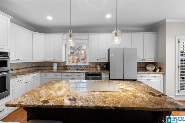 kitchen featuring a kitchen island, stainless steel appliances, crown molding, white cabinetry, and a sink