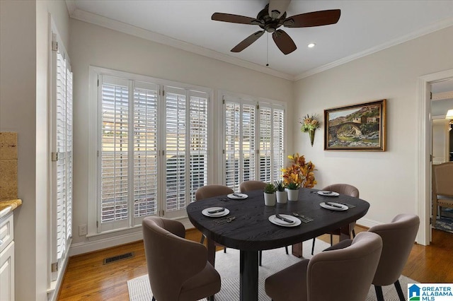 dining room featuring baseboards, light wood finished floors, visible vents, and crown molding