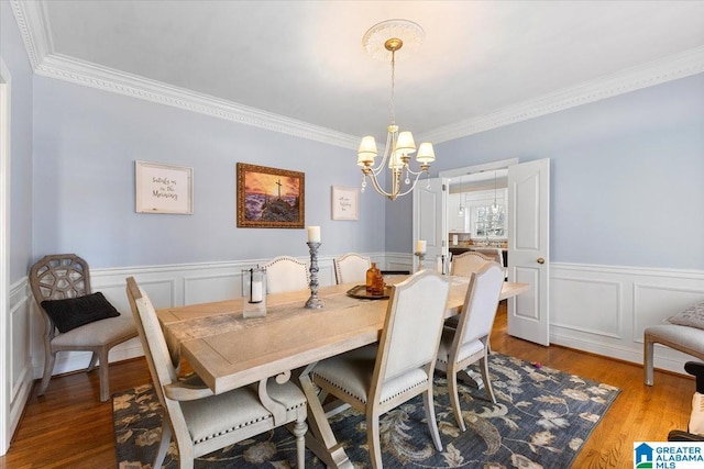 dining room with a wainscoted wall, crown molding, a decorative wall, an inviting chandelier, and wood finished floors