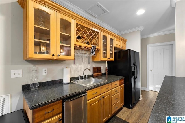 kitchen featuring glass insert cabinets, ornamental molding, wood finished floors, a sink, and black fridge