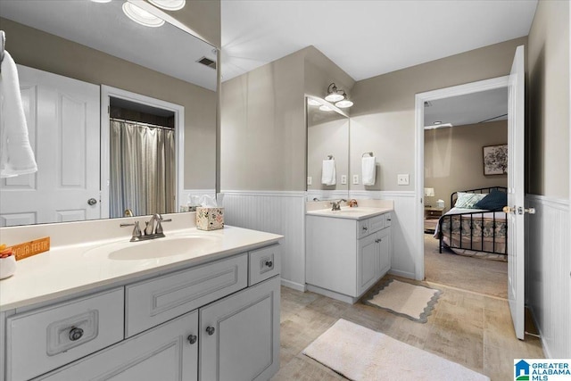 ensuite bathroom featuring a wainscoted wall, visible vents, two vanities, and a sink