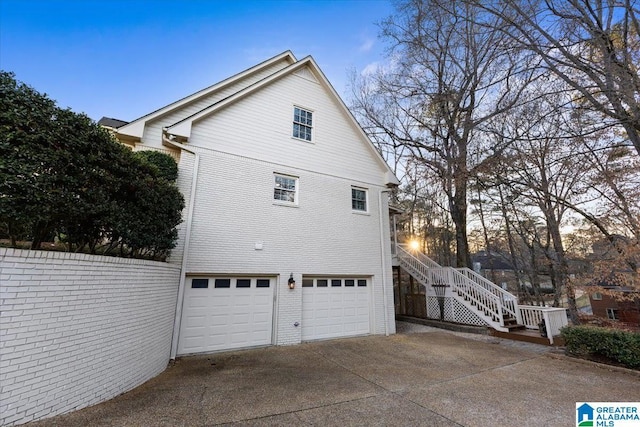 view of side of home featuring stairs, driveway, brick siding, and a garage