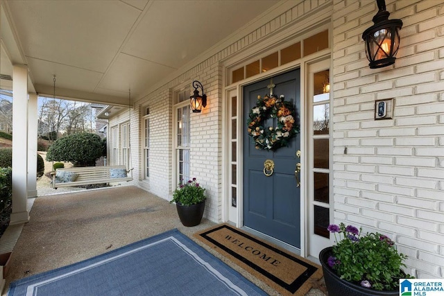 doorway to property with covered porch and brick siding