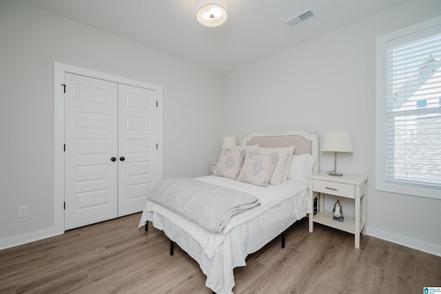 bedroom featuring a closet, wood finished floors, visible vents, and baseboards