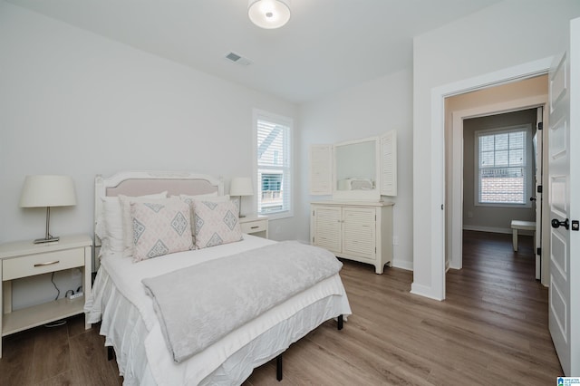 bedroom with wood finished floors, visible vents, and baseboards