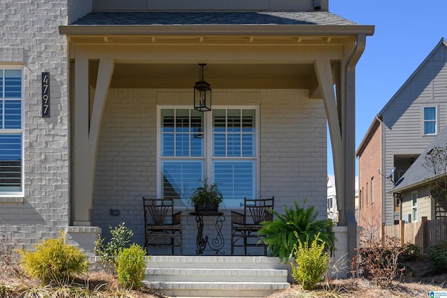 entrance to property with a shingled roof, a porch, and brick siding