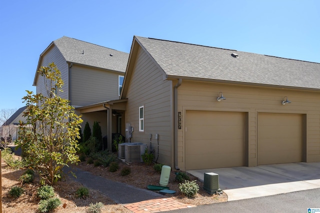 view of side of home featuring a garage, a shingled roof, and central air condition unit