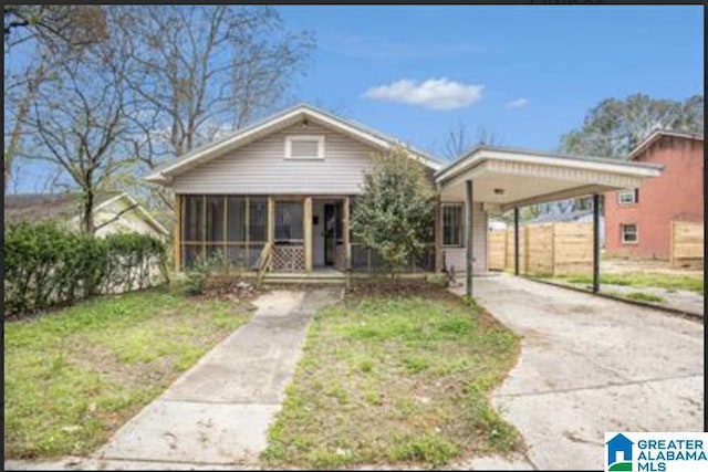 bungalow with concrete driveway, a carport, a front yard, and a sunroom