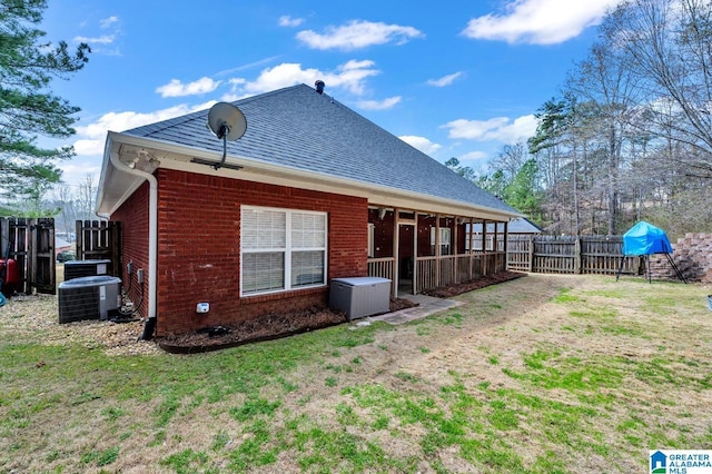 back of house with fence, roof with shingles, central air condition unit, a lawn, and brick siding