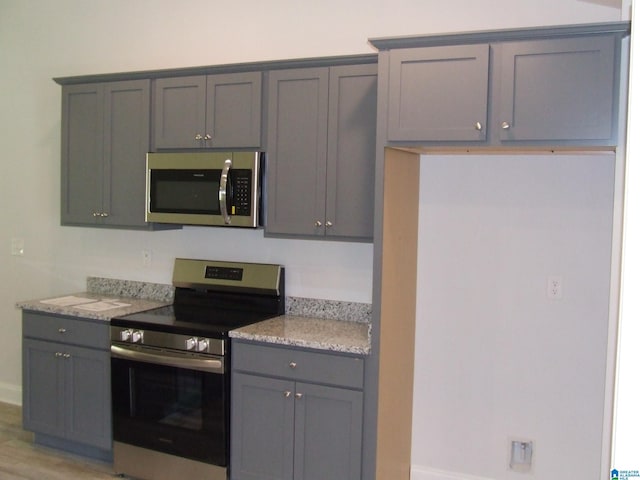 kitchen with light wood-type flooring, gray cabinets, and stainless steel appliances