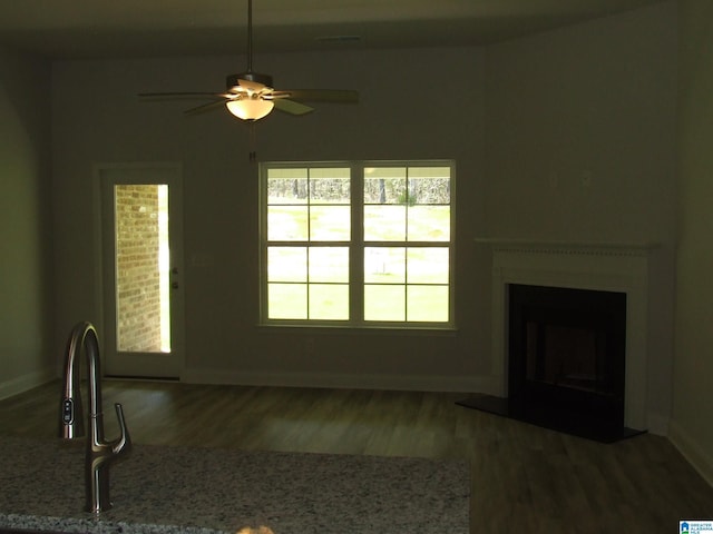 unfurnished living room featuring a fireplace with flush hearth, baseboards, ceiling fan, and wood finished floors