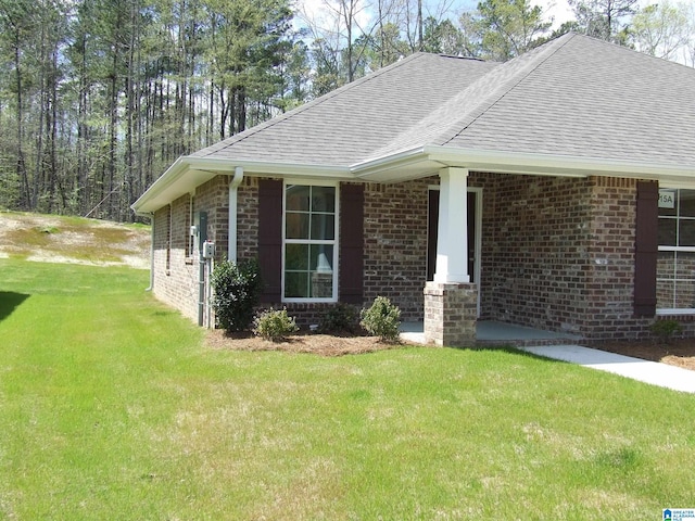 view of side of property with a yard, brick siding, and roof with shingles