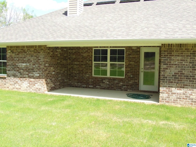 property entrance with brick siding, roof with shingles, a chimney, and a lawn
