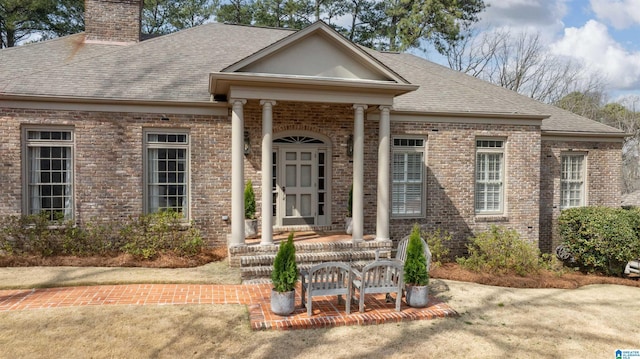 view of front of house featuring brick siding, a chimney, and roof with shingles