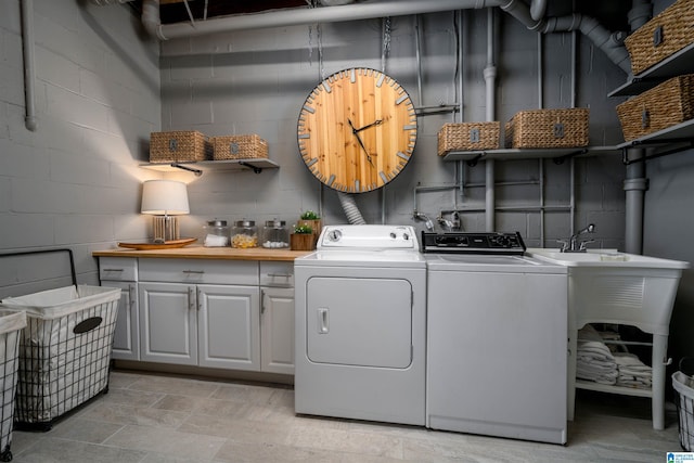 clothes washing area with washer and dryer, concrete block wall, and cabinet space