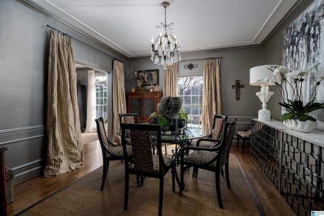 dining space featuring wood finished floors, wainscoting, a chandelier, and ornamental molding