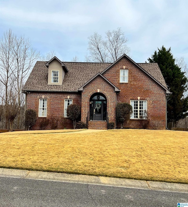 view of front of house with brick siding, a front lawn, and a shingled roof