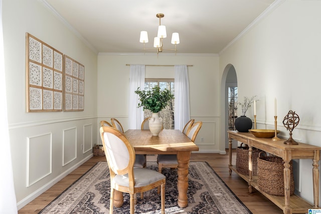 dining room with crown molding, a decorative wall, light wood-type flooring, arched walkways, and a notable chandelier