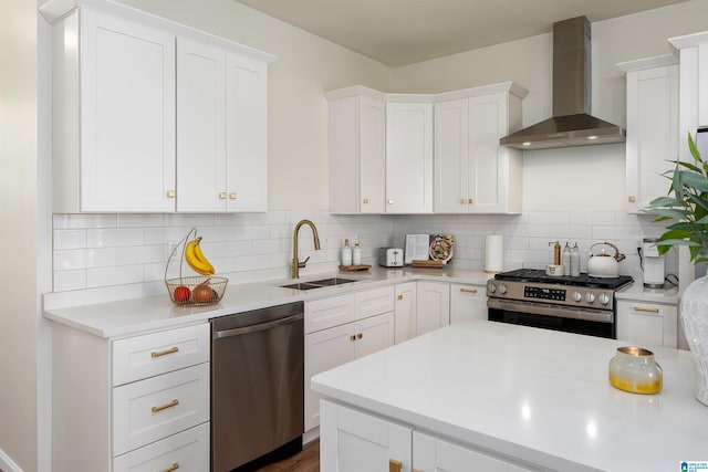 kitchen featuring light countertops, wall chimney range hood, appliances with stainless steel finishes, and a sink