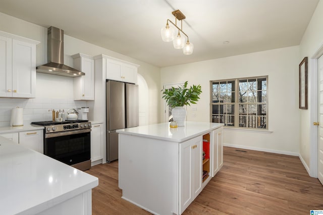 kitchen featuring wall chimney range hood, tasteful backsplash, white cabinets, and stainless steel appliances