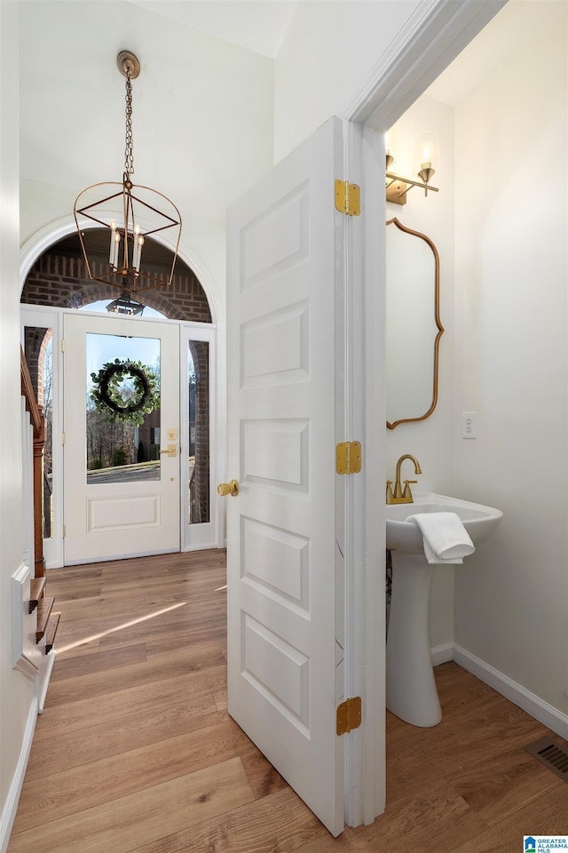 foyer entrance with visible vents, light wood-type flooring, a chandelier, and baseboards