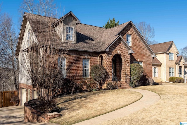 view of front facade with a front yard, fence, a shingled roof, concrete driveway, and brick siding